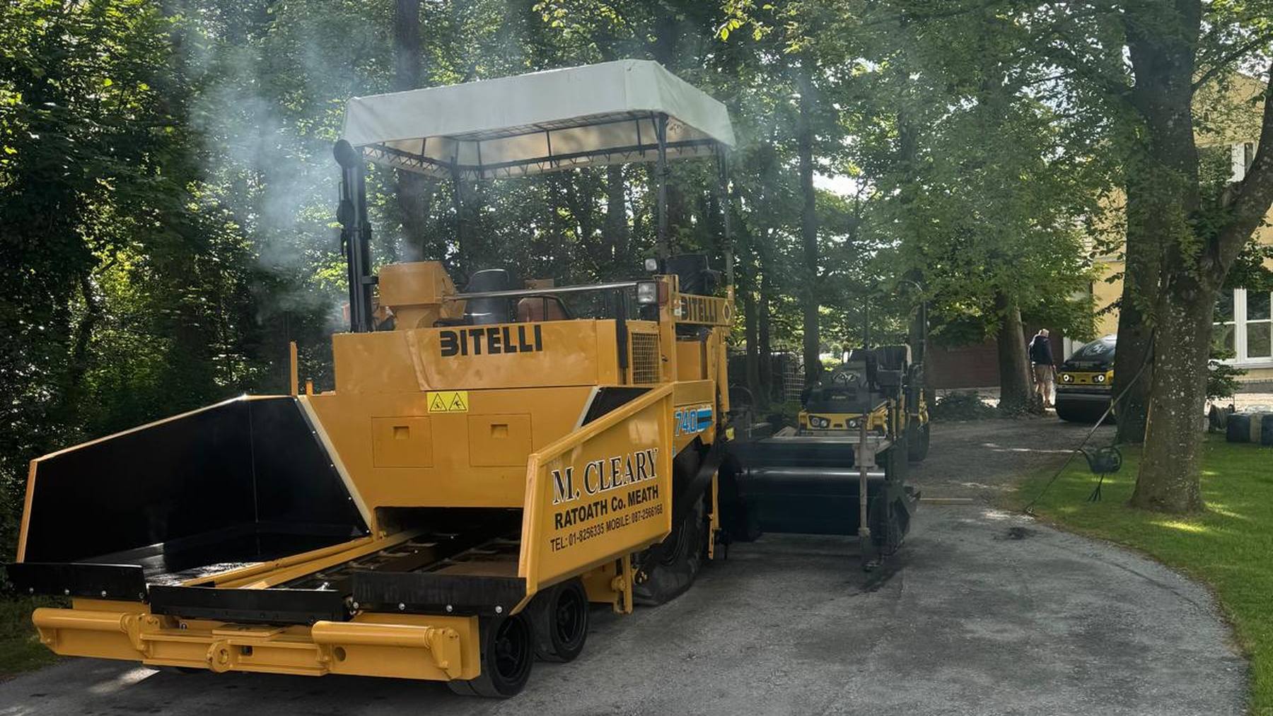 Laying a private driveway under mature trees, steam rising off the fresh asphalt.