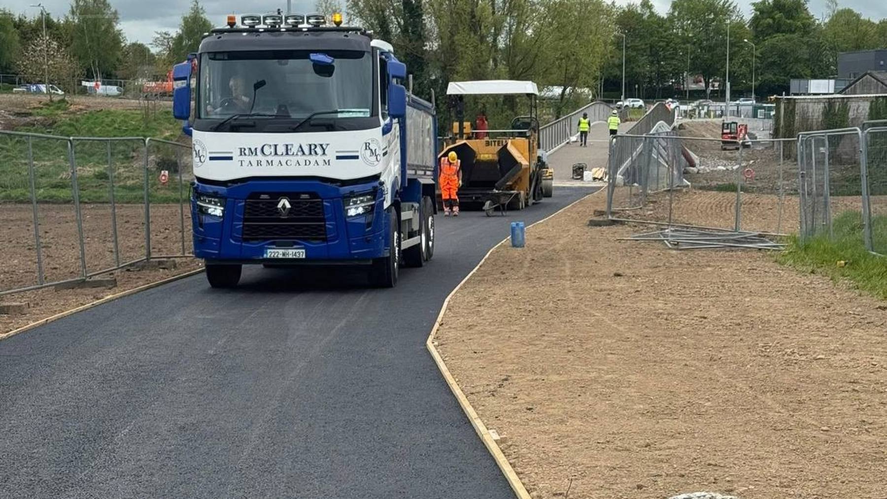 An RM Cleary tipper lorry on a newly surfaced road, with the paver and crew working ahead.