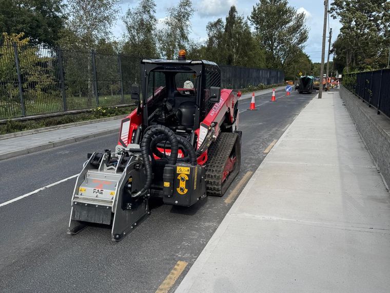 The red RM Cleary Manitou tracked loader on a closed lane with an FAE cold planer head mounted on the front, alongside a newly laid concrete footpath.