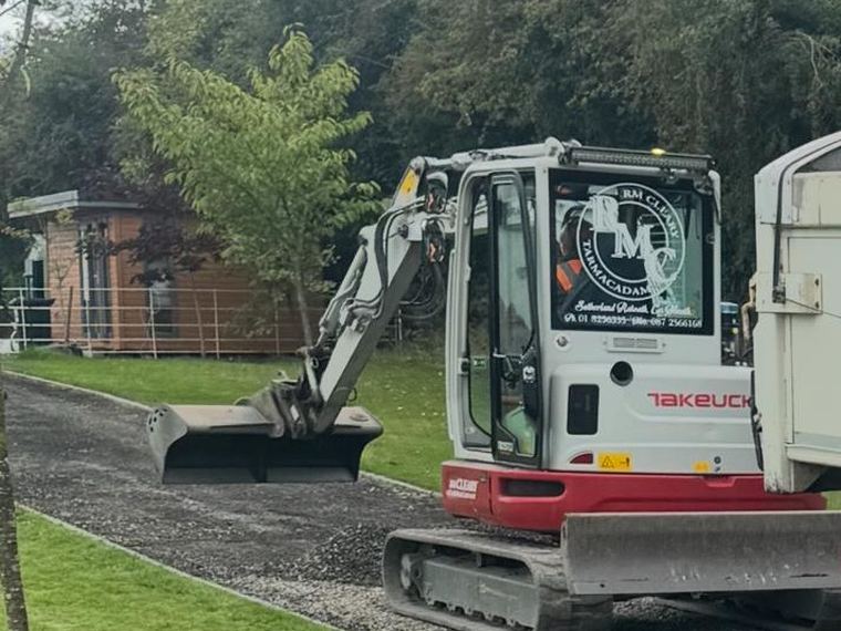 An RM Cleary Takeuchi tracked excavator with a grading bucket, trimming a new gravel driveway to level alongside the lawn.