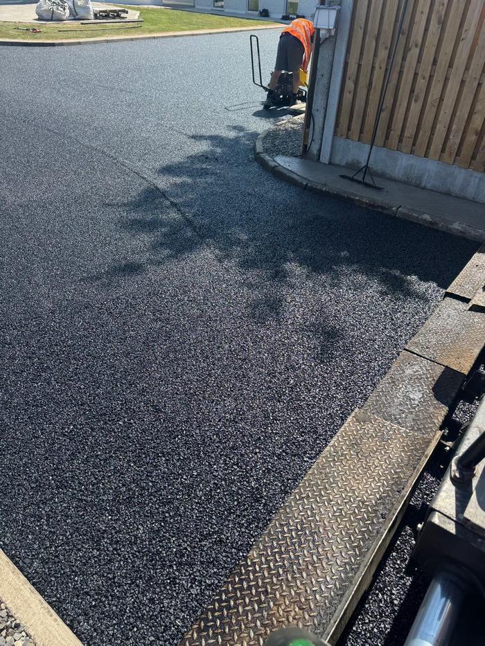 Close view of the fresh surface running up to the side gate, with a crew member compacting the edge by the wall.