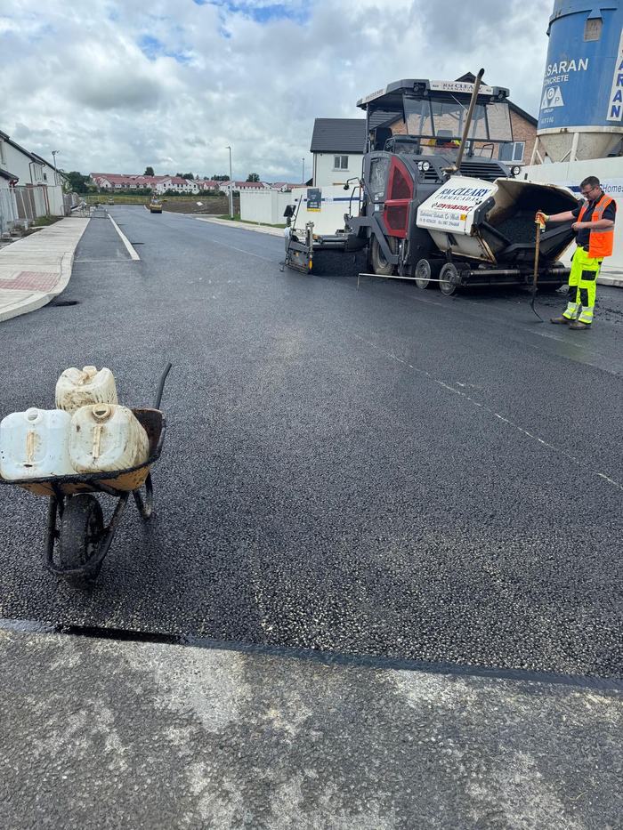 The RM Cleary Dynapac paver laying the wearing course down a new estate road, houses either side.