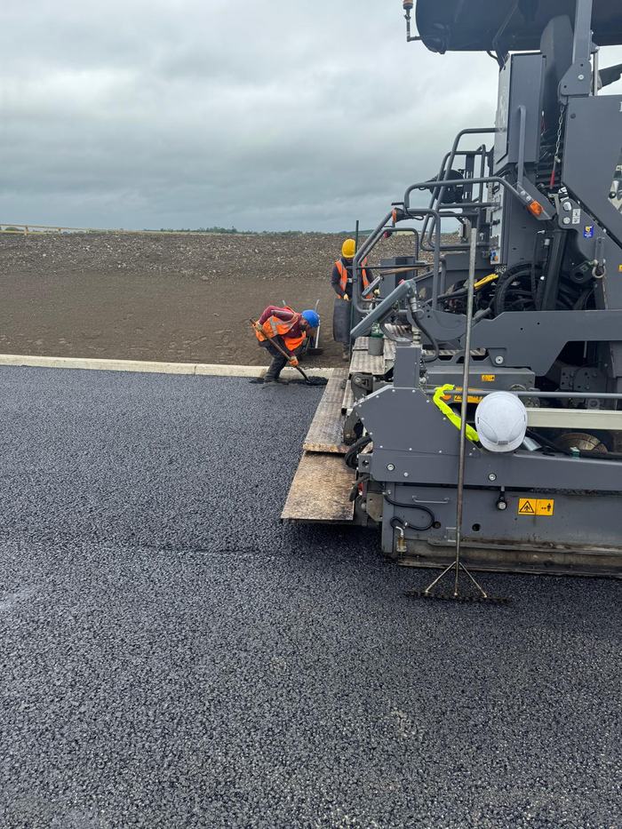 Close view of the paver screed with the crew raking the edge against a new kerb line.