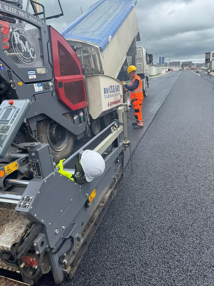 A tipper discharging into the RM Cleary paver hopper with a crew member working the edge.