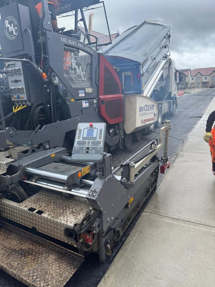 The paver screed working tight to the concrete footpath edge.