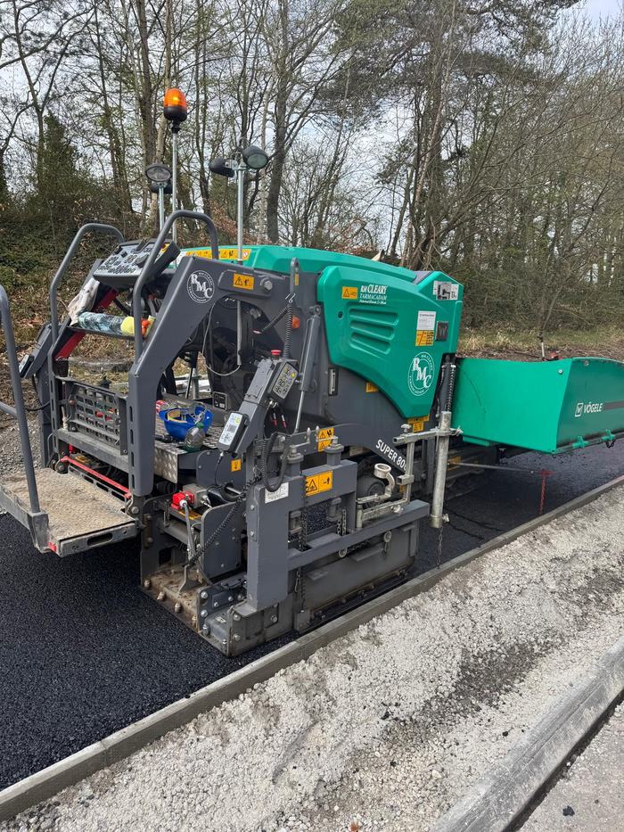 The paver standing on freshly laid asphalt against a newly set concrete kerb line.
