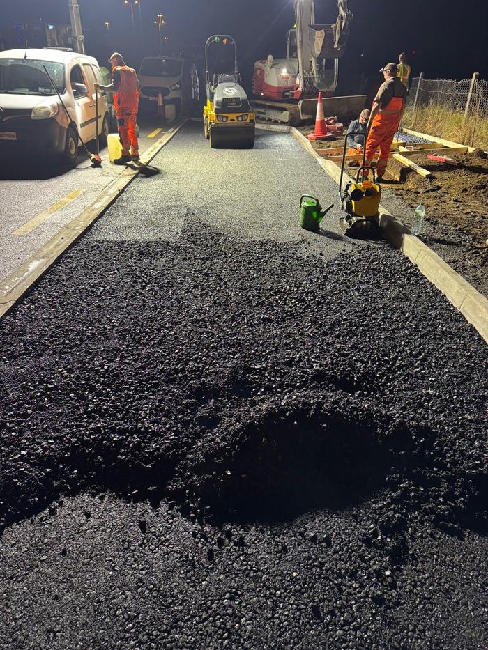 A wide run of fresh black mat under the lights with the crew working the edges behind it.