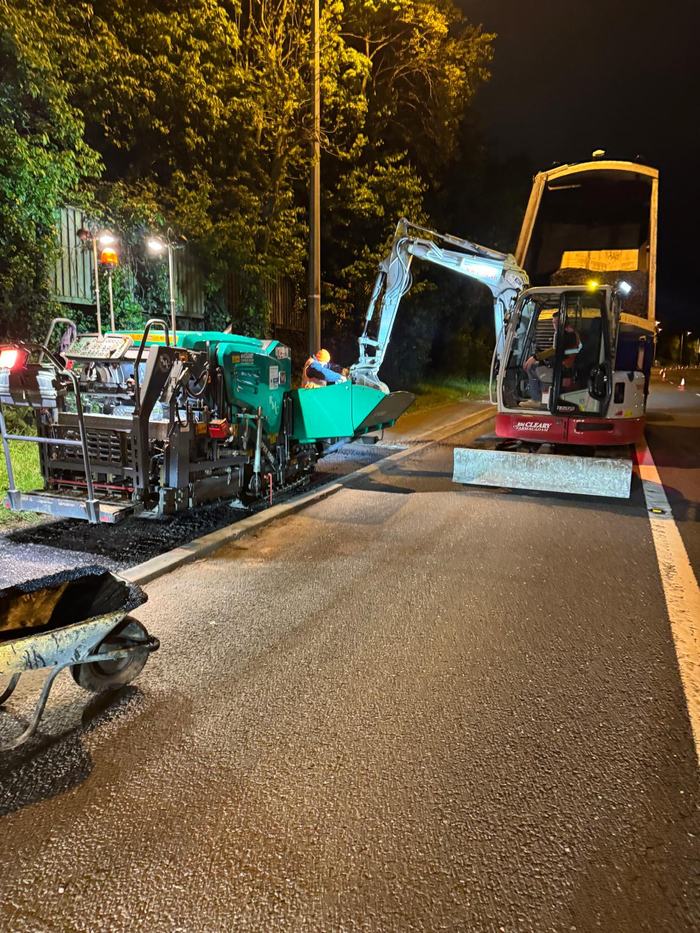 The RM Cleary paver working under lights at night with the tracked excavator alongside, laying up to a new kerb line.