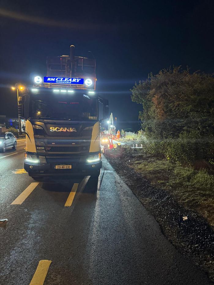 An RM Cleary Scania tipper on the closed lane with the works lit up behind it.