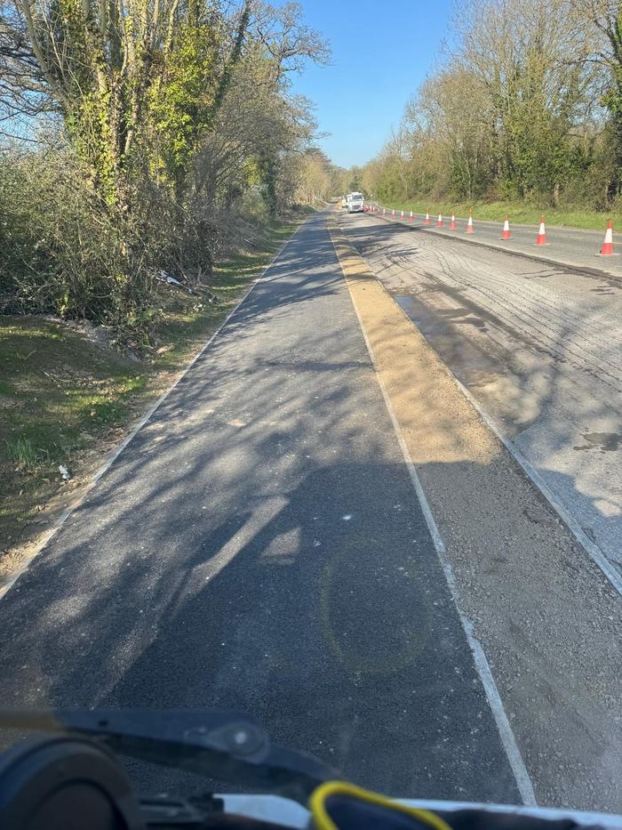 The finished lane seen from the paver, kerbed and lined, with the works still coned off.