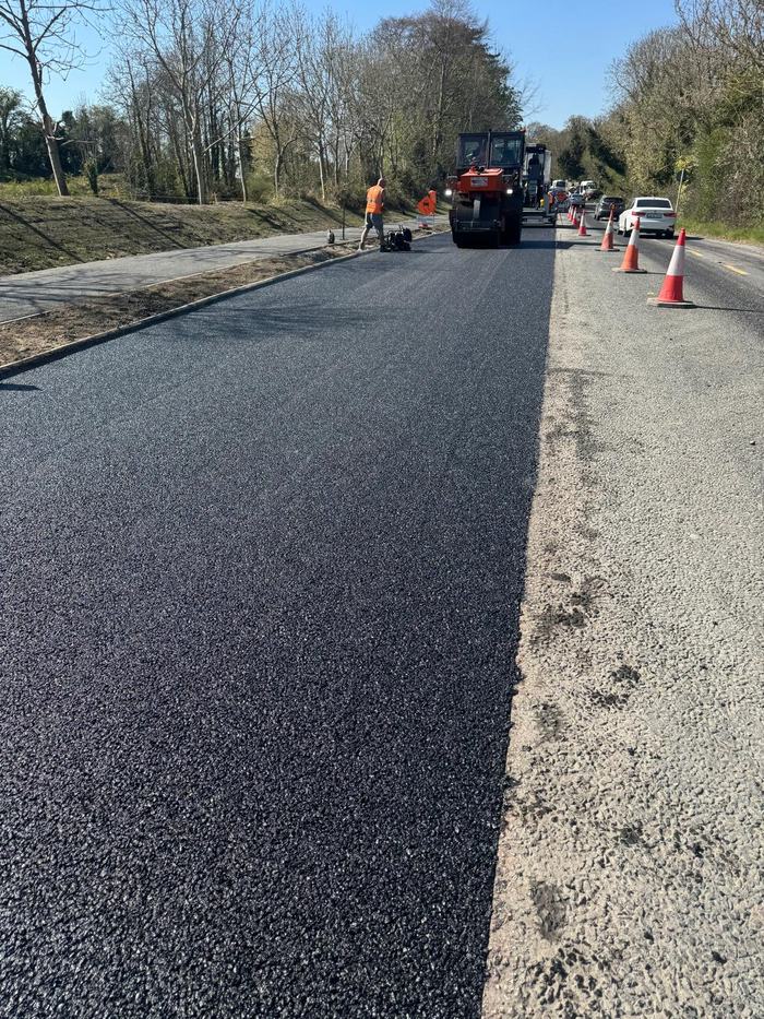 The newly laid mat running away between the trees with the roller working ahead, under traffic management.