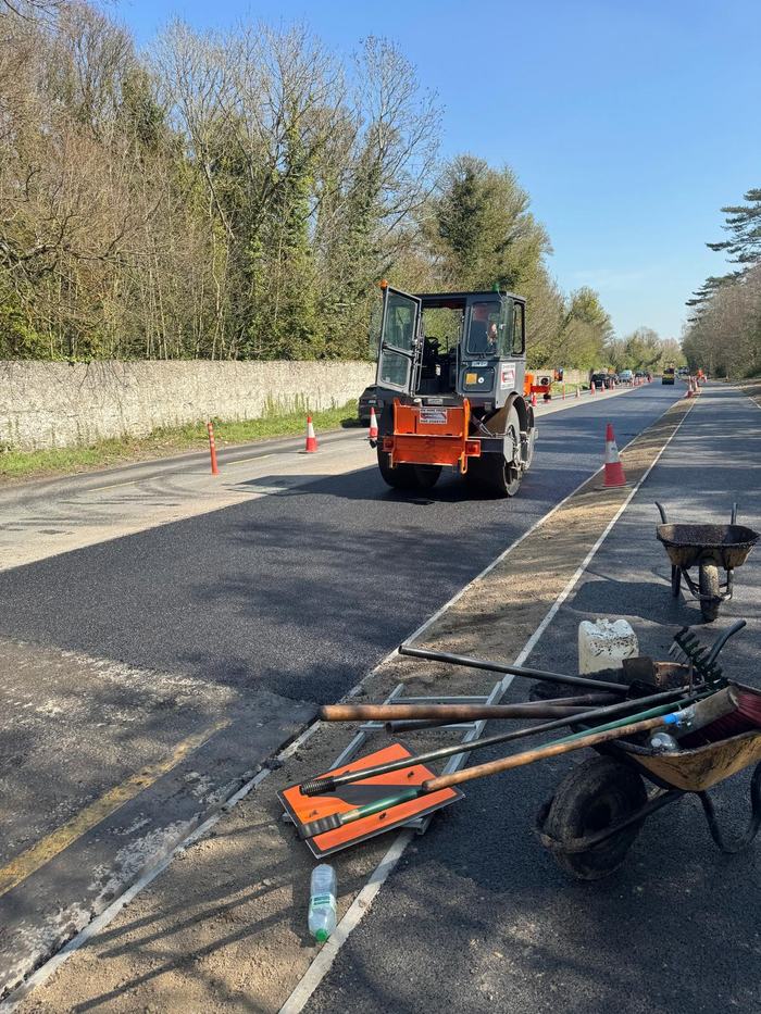 The roller finishing a wide section of carriageway with the crew tools laid out on the verge.