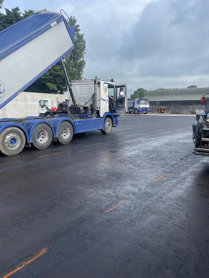 A tipper discharging into the paver on the prepared surface, with the second lorry waiting behind.