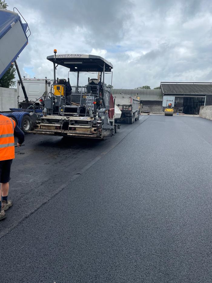 The paver laying alongside the sheds with tippers feeding and the roller following behind.